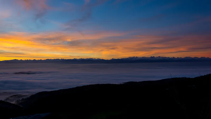 Morgendämmerung über dem Nebelmeer, dahinter die Alpenkette